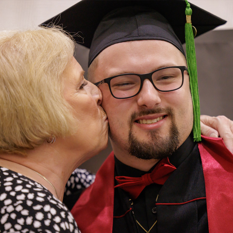 An older woman kisses a smiling graduate on the cheek